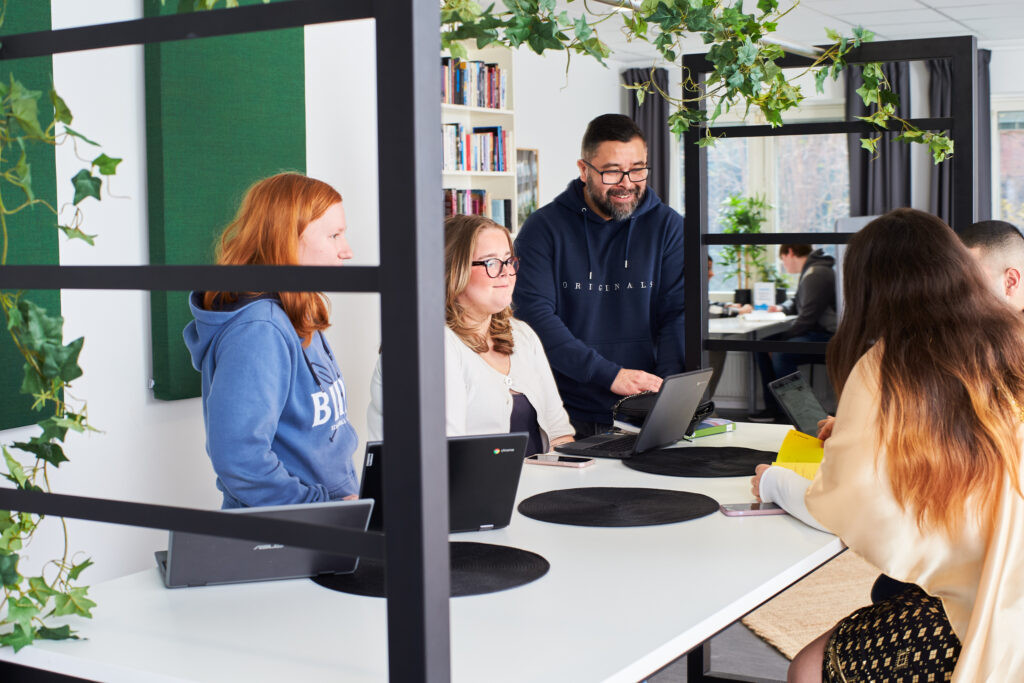 Elever sitter runt ett bord i skolan med en lärare bredvid